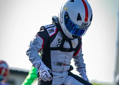 Ethan stepping out of his kart number 47 after a race. Wearing his white & black race suit, white helmet with red vertical stripe, and OMP sponsor branding